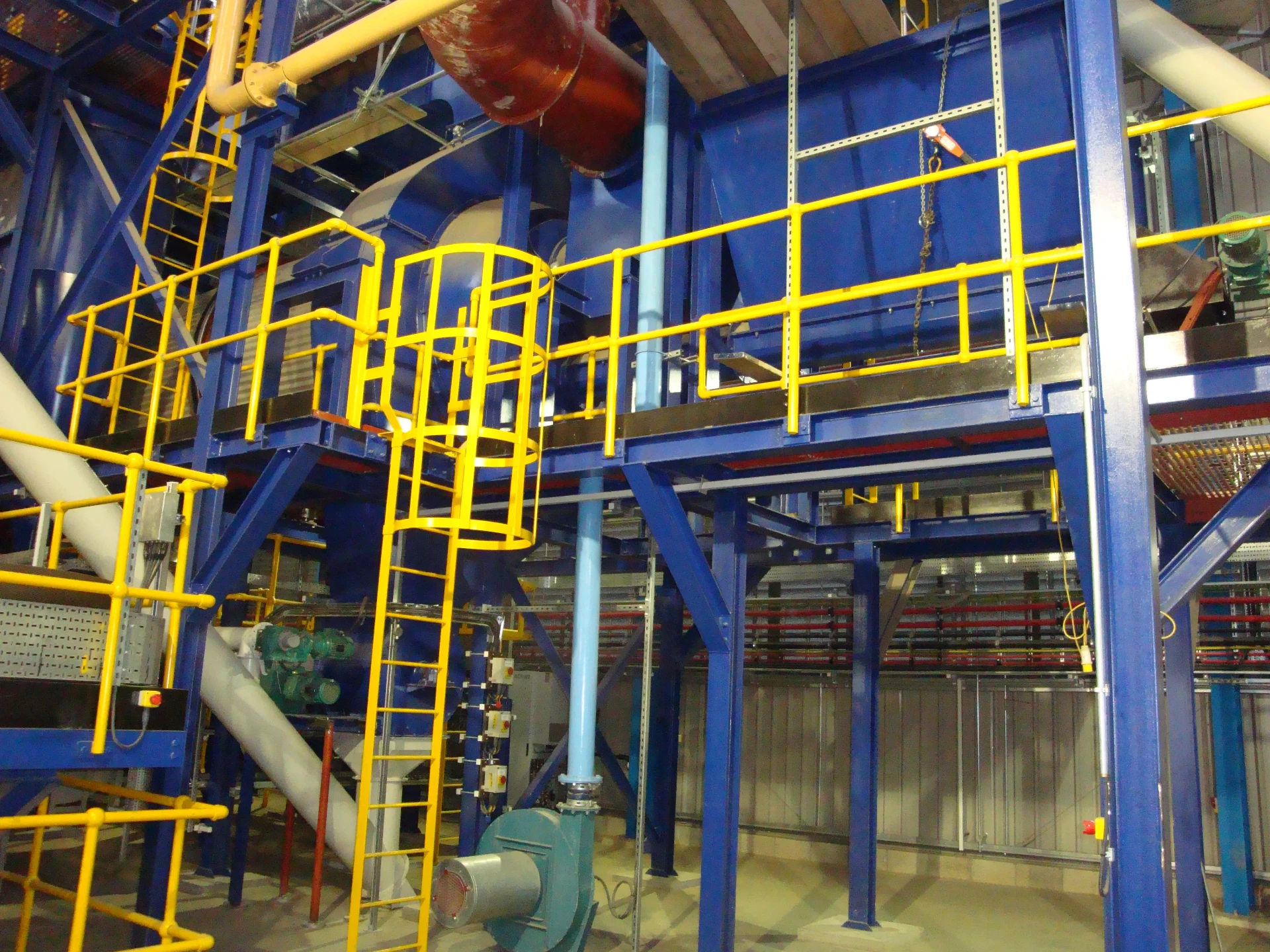 Blue processing plant interior with yellow safety railings and piping